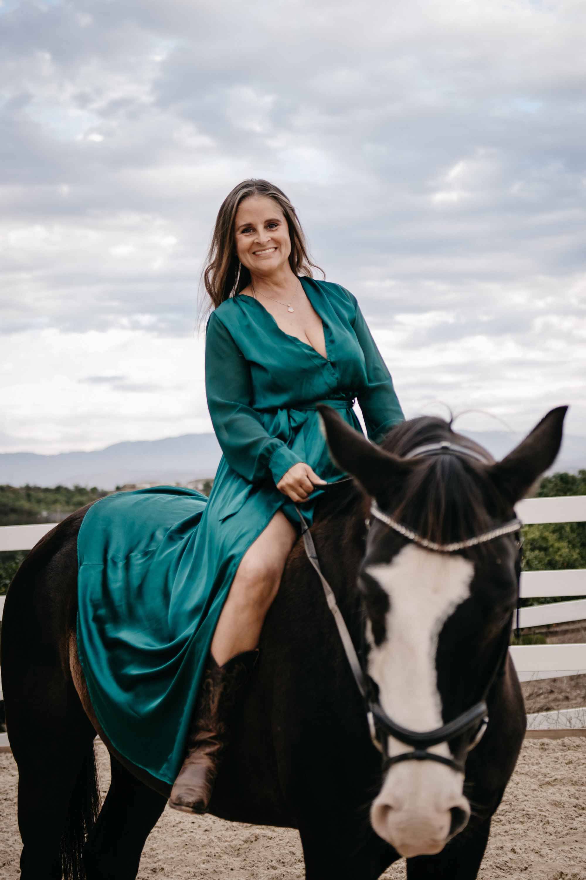 Image of a woman in a green dress on a white and brown Hanoverian horse.