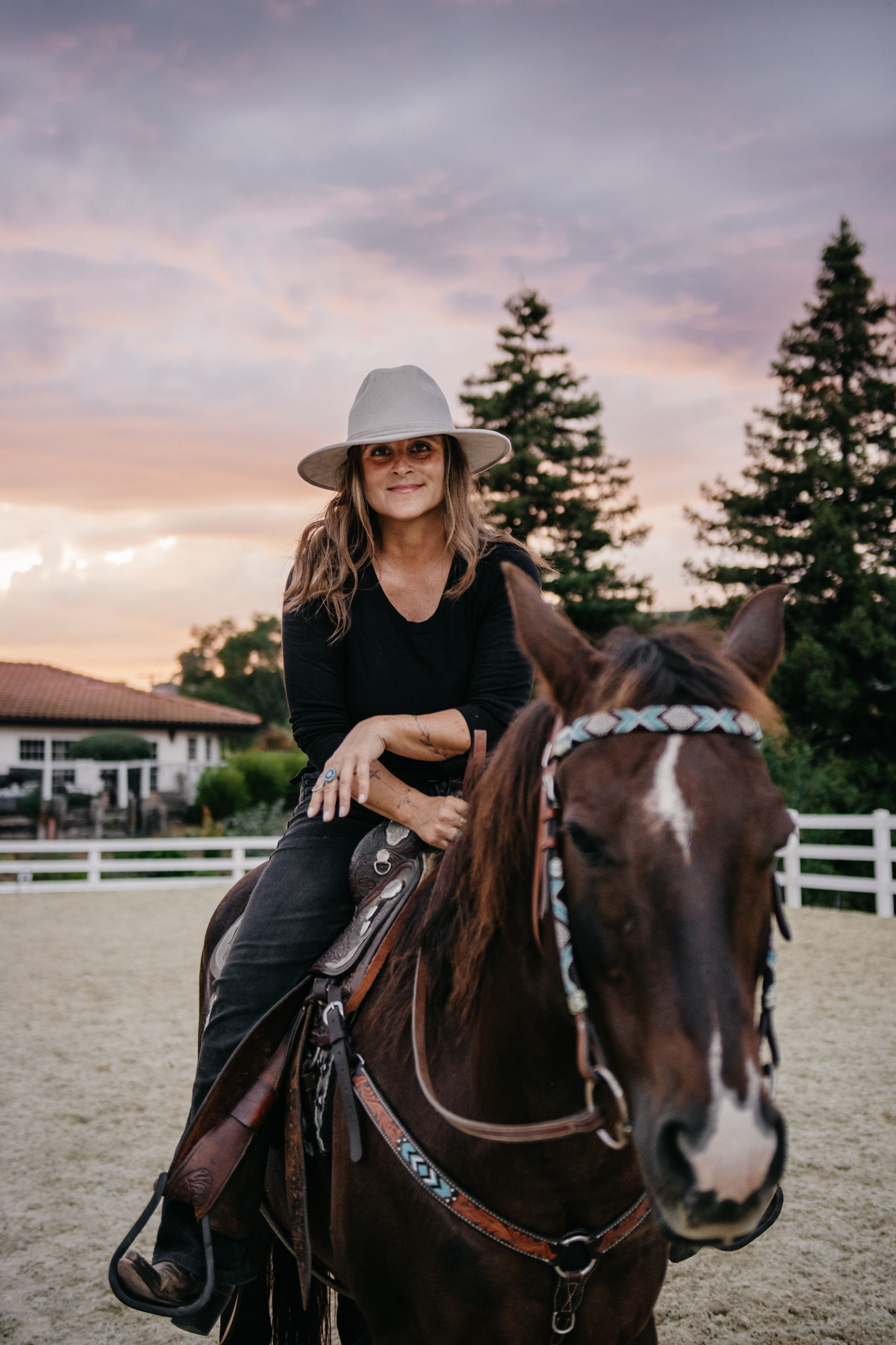 Image of a woman in a cowboy gate leaning on the pommel of her horse's saddle.