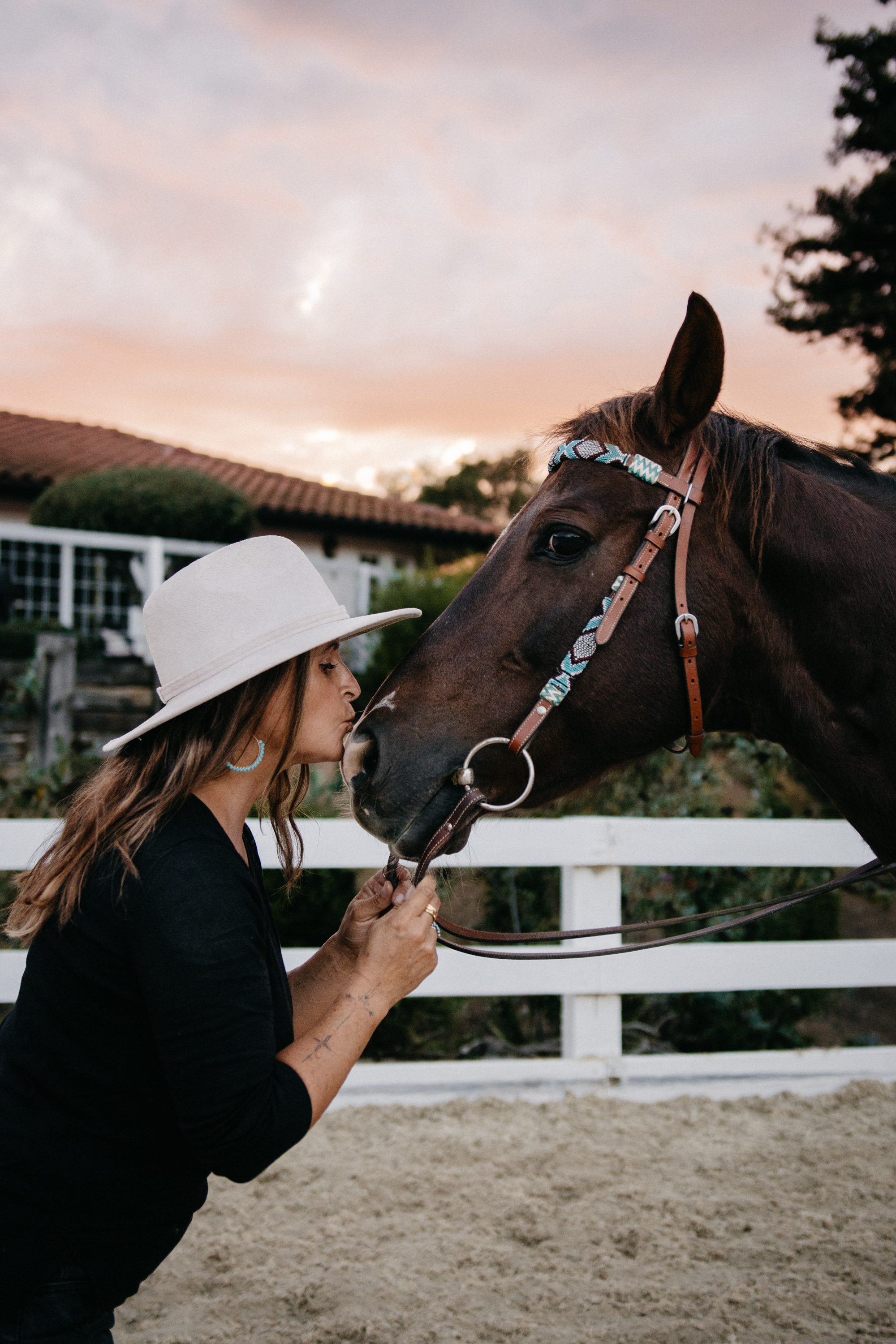 Image of a woman in a cowboy hat giving her horse a kiss.