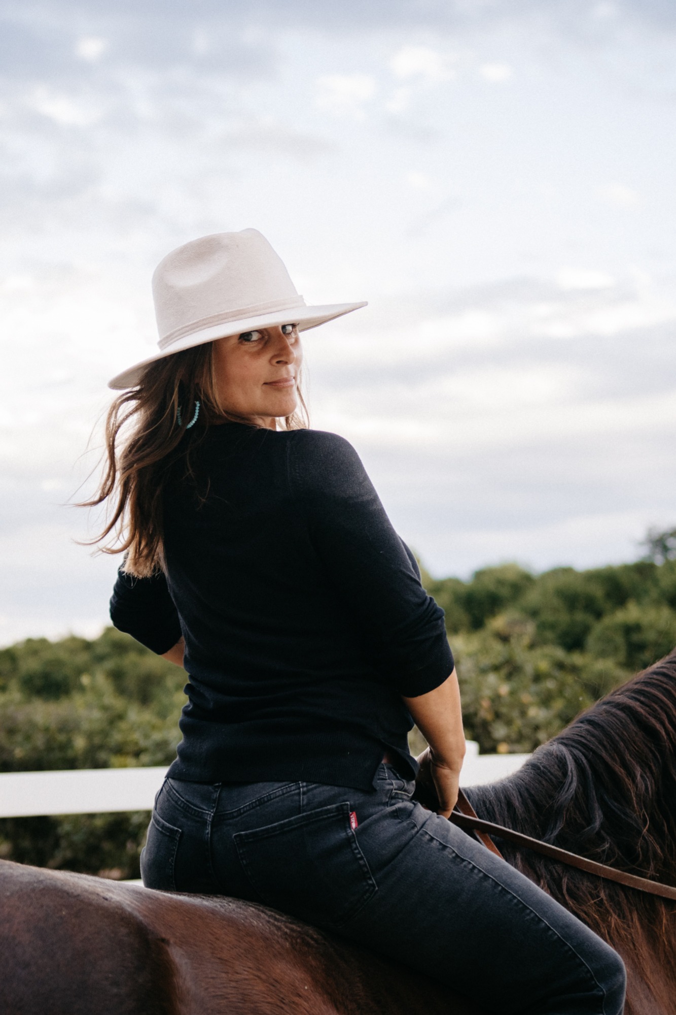 Image of a woman in a cowboy hat riding a horse and looking over her shoulder.